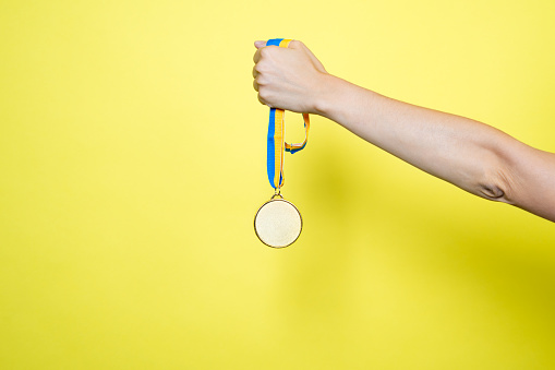 Hand hold Gold medal on yellow blue ribbon isolated on yellow background. Medal mockup.