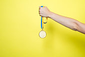 istock Hand hold Gold medal on yellow blue ribbon isolated on yellow background. Medal mockup 1426888167