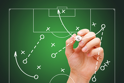 Football soccer coach drawing game playbook, strategy and tactics with white marker on transparent wipe board.