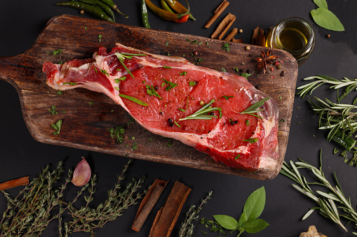 Raw lamb leg on blue stone background with herbs.