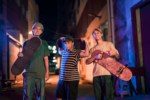 portrait diversify young men standing at back alley holding skateboard looking at camera smiling
