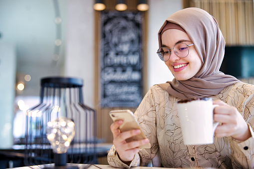 Hijabi girl using a mobile phone to surf through the social media posts