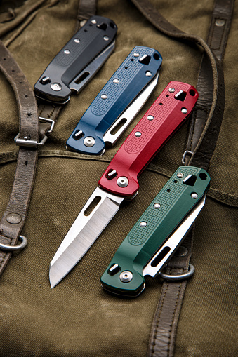 Folding multitool penknives on a khaki canvas backpack. A pocket-sized tool for hiking and daily life.