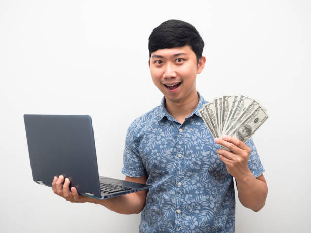 Asian man blue shirt holding laptop with a lot of money excited face isolated Asian man blue shirt holding laptop with a lot of money excited face isolated clock wall clock face clock hand stock pictures, royalty-free photos & images