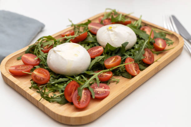 queijo buratta tradicional fresco com folhas de rúcula e tomate cereja em uma bandeja de madeira. queijos italianos - buratta - fotografias e filmes do acervo