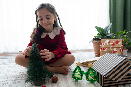 Cute girl sitting and decorating small Christmas tree