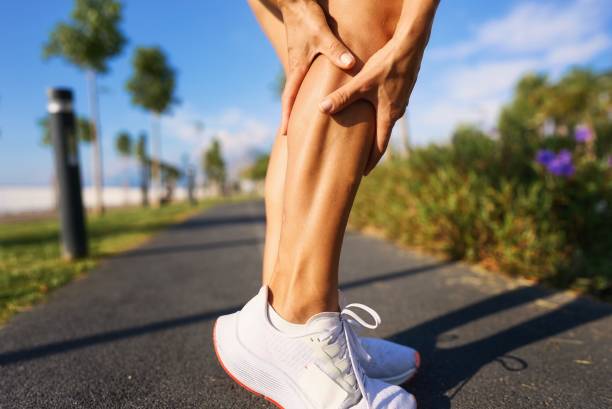 Caucasian female runner sport woman has leg cramp while she is running on beach in morning stock photo