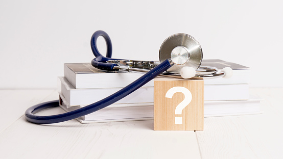 wooden block with white question mark, stethoscope, book, notepad on white wooden table. medical and education concept.