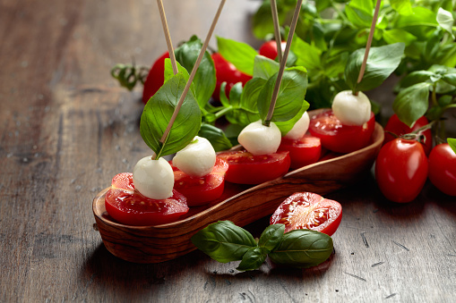 Mozzarella with basil and tomatoes on an old wooden table. Traditional Italian snack.