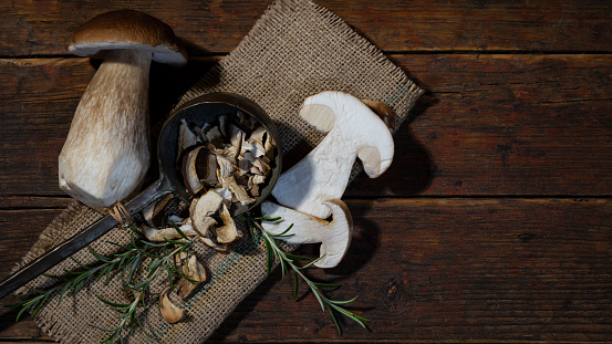 Dark food photography background - Forest mushrooms / Boletus edulis (king bolete) / penny bun / cep / porcini / mushroom and rosemary herbs on jute sack on table, top view