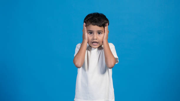 istock happy child with blue background, pointing touching his cheeks in surprise 1426949538
