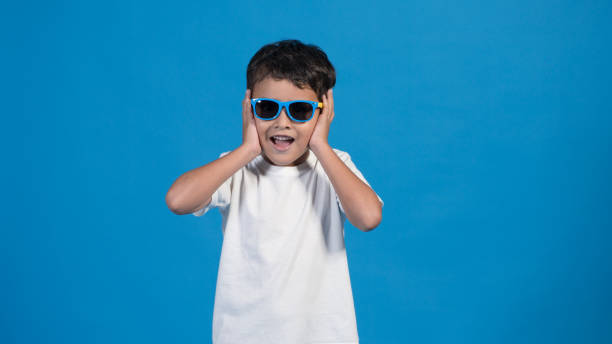 istock happy boy with glasses and blue background, pointing touching his cheeks in surprise 1426949542