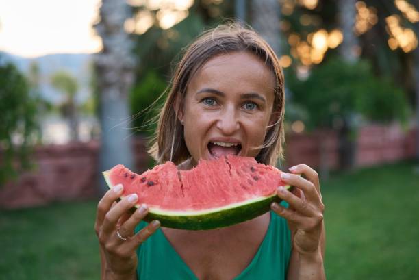 Close up of excited young girl in summer spending time at the park, biting slice of a watermelon stock photo