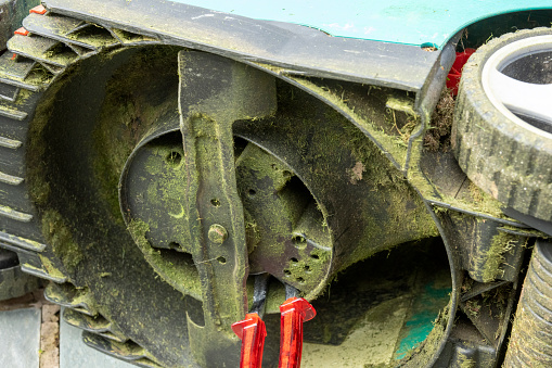 The underside of a rotary lawnmower.  The blade is dull and in need of sharpening the tools are to stop it rotating as the nut is slackened.