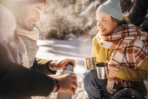 Man and woman, father and his adult daughter drinking hot tea in nature together during winter days.
