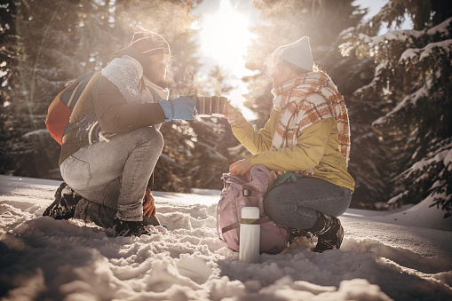 Man and woman, father and his adult daughter drinking hot tea in nature together during winter days.