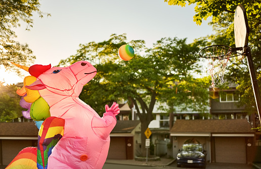 Person wearing an inflatable unicorn costume playing basketball on street court outdoors on a sunny day