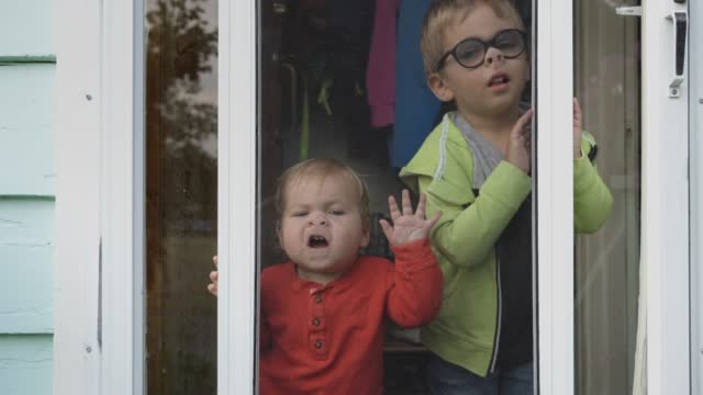 Cute young boys pressing their faces against their front door