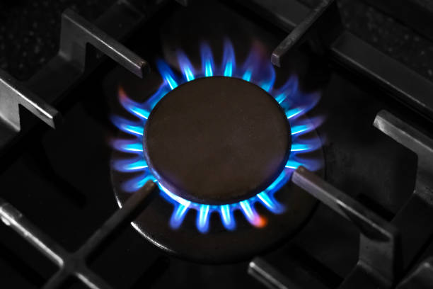 Gas burner with a blue flame on a black kitchen stove, with a cast-iron grate, top view, selective soft focus. gas crisis