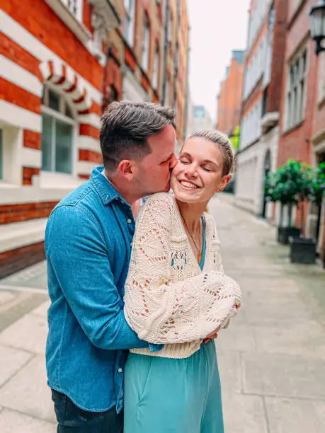 Candid Portrait of Cute Caucasian Male and Female Tourists Posing Together and Kissing in a Vibrant-Colored Alley in London, England