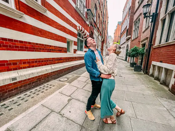 Candid Portrait of a Cute Caucasian Male and Female Standing and Laughing Together While on Vacation in a Vibrant-Colored Alley in London, England