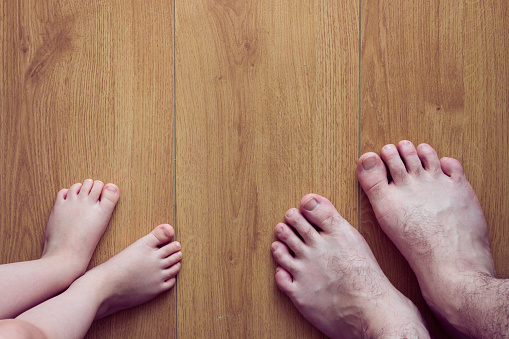 Top view of father and daughter's feet on wooden background. Caucasian little girl and man's feet. Father's day concept with copy space design.