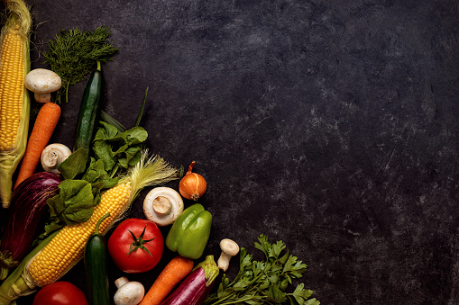 Fresh ripe organic vegetables and mushrooms on the left corner on black background. Healthy eating concept. Dark low key photo. Top down view. Flat lay composition. Copy space.