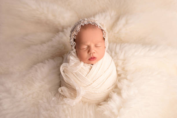 istock Sleeping newborn girl in a white cocoon with a white cap on a white background. Studio macro photography, portrait of a newborn. 1426974045