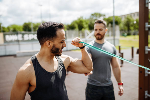 istock Fitness instructor and Latin trainee on outdoor training. Men exercising with strong rubber strip 1426974243