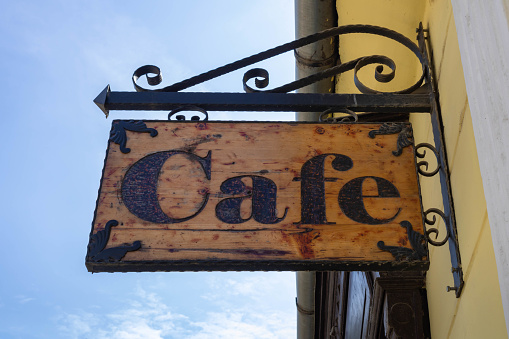 An old wooden rustic board hanging on the wall with the cafe inscription, outdoors, blue sky background
