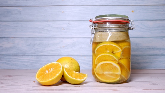 Fermented oranges in a fermentation jar against a blue wooden background