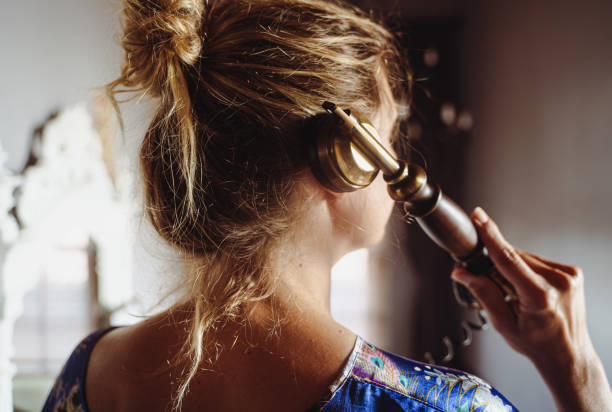 ritratto posteriore di donna con i capelli biondi che parla al telefono vintage nella luce intima della stanza interna - landline phone women close up old fashioned foto e immagini stock