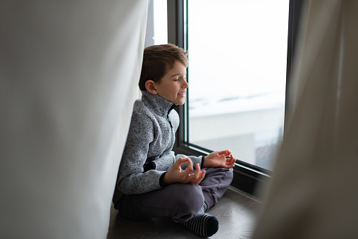 Beautiful boy meditating on a winter vacation, near the window.