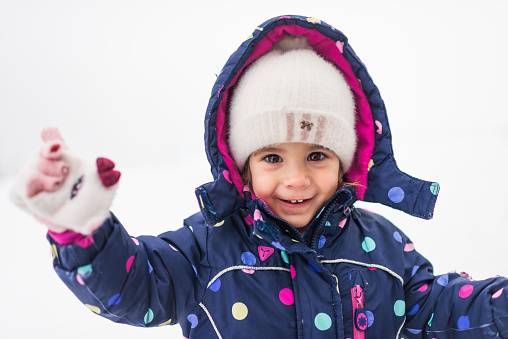 Happy cheerful child play with snow in winter outdoors in park, in forest. Active family leisure with children in winter on cold days in vacations. Girl playing snowballs