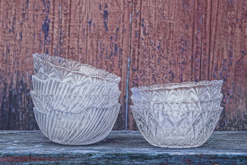 a set of white glass crystal plates of salad bowls stand on a gray table against a wooden wall