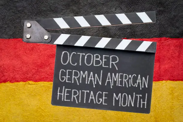 October - German American Heritage Month, white chalk text on a clipboard against paper abstract in colors of Germany national flag, reminder of cultural event