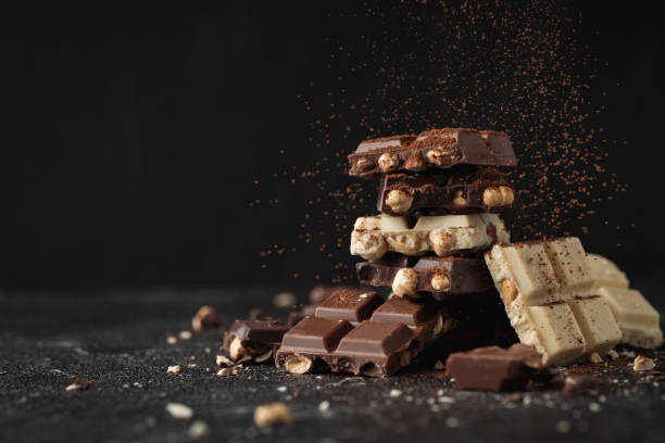 istock White, Milk and Dark square chocolate bars crushed with nuts on the black background and sprinkled with cocoa powder 1426998537