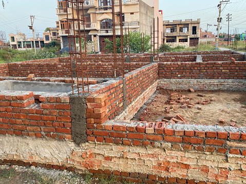 Stock photo showing close-up view of an Indian red brick construction building site that employs female labourers. Approximately 15 million women work as unskilled labourers in India's construction labour force. They are employed because they are paid less than men to do tasks such as dust lifting, digging and brick handling.