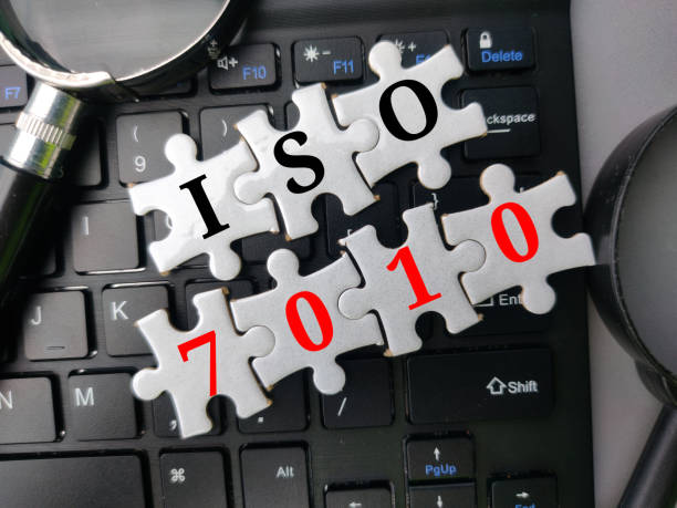 ワイヤレスキーボード上の単語iso 7010とトップビューパズルと虫眼鏡。ビジネスコンセプト。 - construction environment factory fire ストックフォトと画像