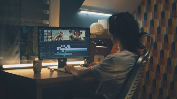 Male editor working on video on pc Male editor in headphones sitting at the table at night and editing video with astronauts for customer on pc in professional program while working remotely editing equipment stock pictures, royalty-free photos & images