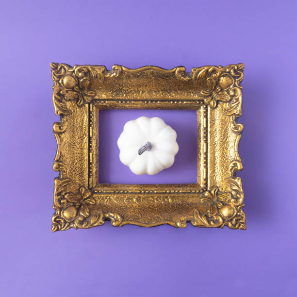 istock A white pumpkin in a vintage golden frame against lilac background. Minimal creative concept for Halloween celebration invitation or banner. Autumn wallpaper 1427010505
