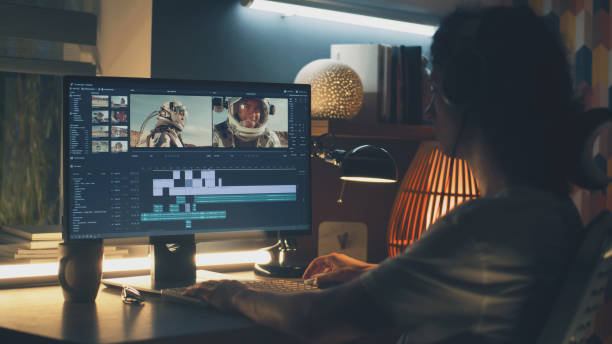 Male editor working on video on pc Male editor in headphones sitting at the table at night and editing video with astronauts for customer on pc in professional program while working remotely female film editor stock pictures, royalty-free photos & images