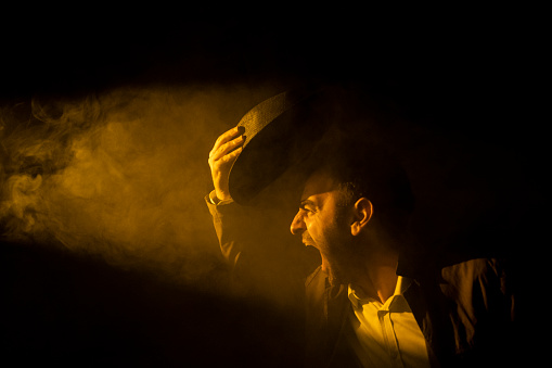 portrait of man taking off his hat and shouting against the light