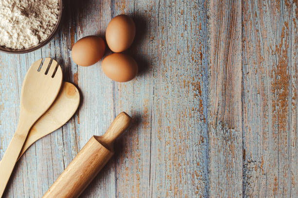 overhead shot on weathered wooden work table with eggs, whisk, rolling pin, flour. Copy space on the right