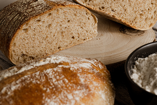 close-up photo of several artisan breads cut from wholemeal flour with a jar of flour on a rustic wooden table