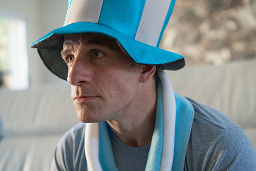 Close-up  of  an argentine man wearing a hat is sitting on a sofa and tensely watching a soccer world cup match at his home