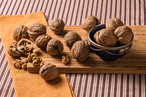 Set of fresh walnuts just picked from the tree on a wooden board and clay bowl painted blue Arabic style. All about burgundy and brown striped tablecloth