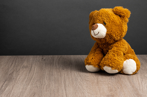 Front view of a teddy bear on table with dark background. Space to write, useful work space.