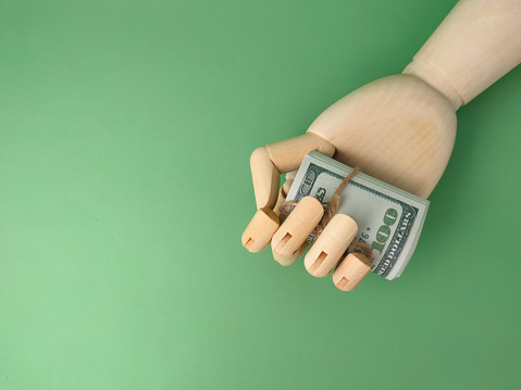 Wooden hand holding banknotes on a green background with copy