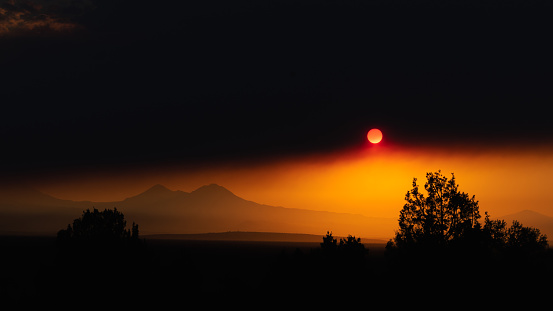 The orange sun shines through a layer of smoke before falling behind the horizon line.